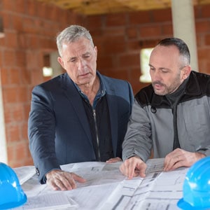 Two men reviewing construction plans, representing contractor liability for subcontractor wage issues.