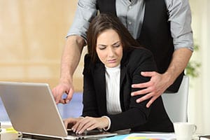 Man engaging in inappropriate behavior towards woman at her desk, representing sexual harassment