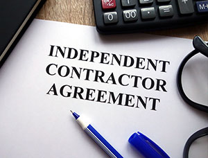 Close-up of an INDEPENDENT CONTRACTOR AGREEMENT document with a pen, glasses, and calculator nearby.